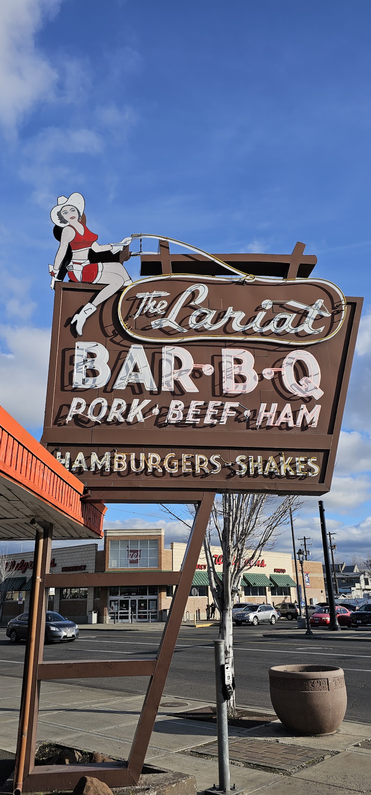 The vintage neon cowgirl-and-lasso sign at the Lariat Bar-B-Q against a blue Yakima sky
