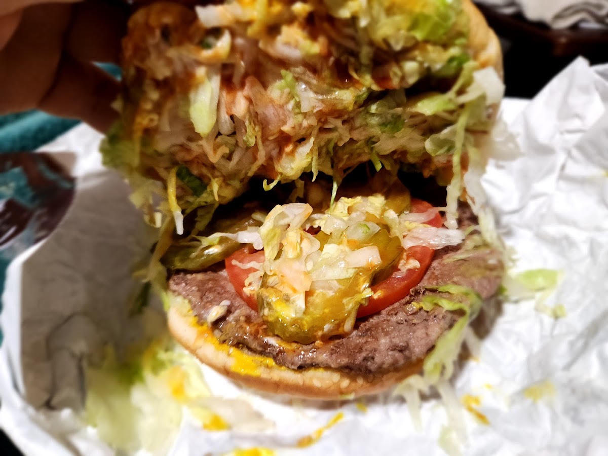 A loaded Lariat burger held in hand, stacked with lettuce, tomato and jalapeno
